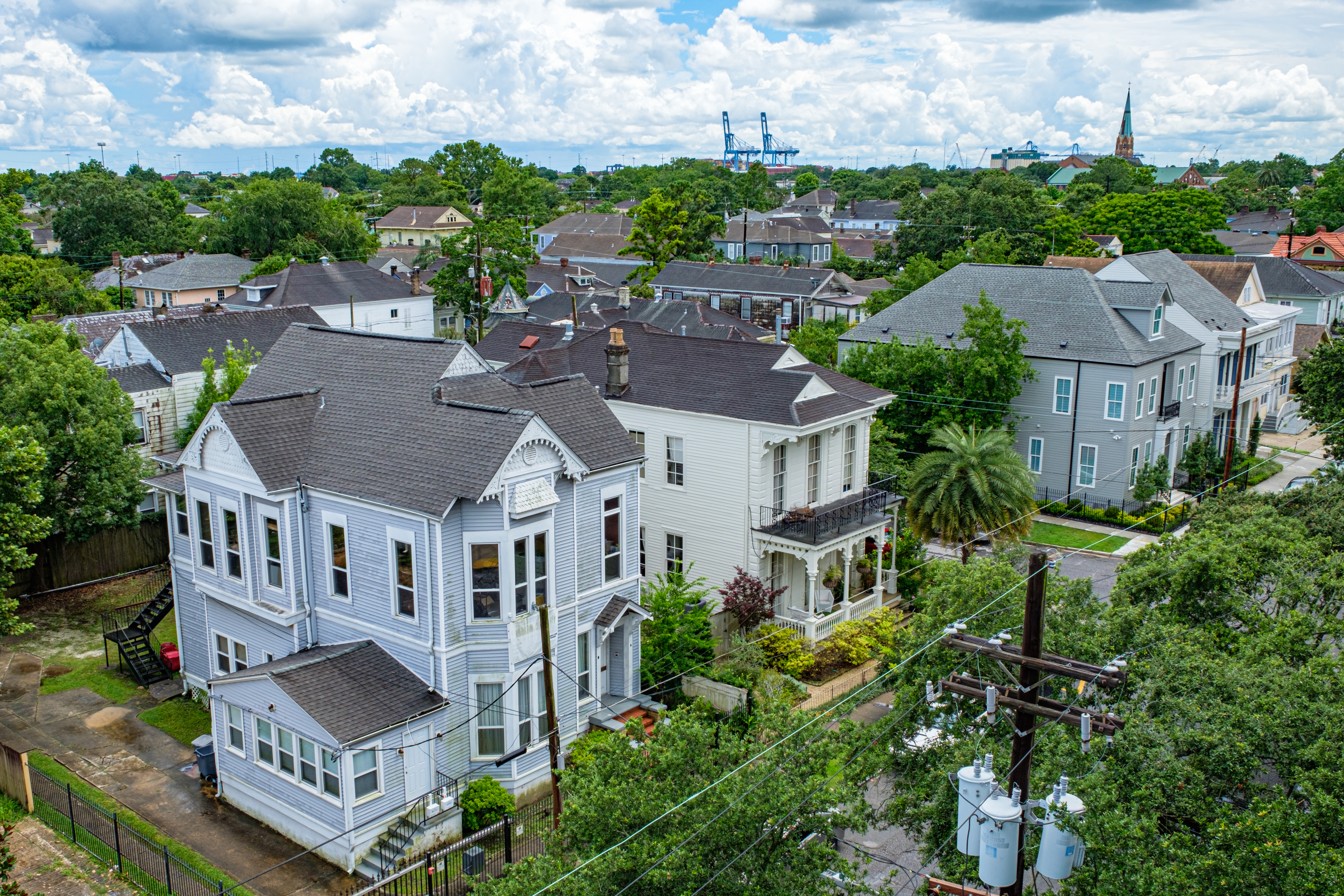 Aerial view of old homes and church steeple in Uptown Neighborhood on Prytania Street with shipyard cranes on the Mississippi River in the background in New Orleans, LA, USA